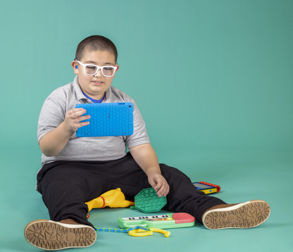 A little boy watching on his tablet surrounded by toys